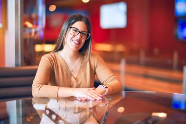 Mutlu ve kendinden emin gülümseyen genç ve güzel bir kadın. Barda gülümseyerek oturmak.