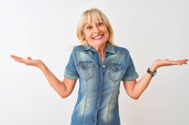 Sıradan bir kot gömlek giyen orta yaşlı bir kadın soyutlanmış beyaz arka plan üzerinde duruyor. Kolları ve elleri havada, kafası karışmış bir ifade. Şüphe kavramı.