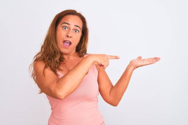 Orta yaşlı olgun bir kadın, beyaz izole edilmiş arka planda durup hayrete düşmüş ve kameraya gülümserken eliyle ve parmağıyla işaret ediyor..