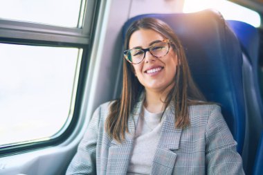 Mutlu ve kendinden emin gülümseyen genç ve güzel bir kadın. Yüzünde gülümsemeyle oturmuş trenle seyahat ediyor.