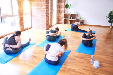 Genç ve güzel bir grup sporcu kadın yoga yapıyor. Spor salonunda spor yapan kadınlara esneme hareketleri öğreten koç.