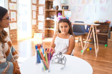 Anaokulunda bir sürü oyuncağın etrafında tek boynuzlu at diademi takan güzel öğretmen ve bebek.