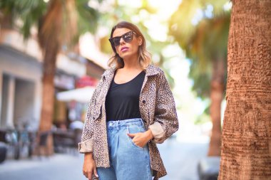 Güneş gözlüğü takan genç ve güzel bir kadın mutlu ve kendinden emin gülümsüyor. Şehir caddesinde ayakta ve yürüyorum.