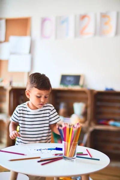 Beautiful toddler boy drawing cute draw using colored pencils at kindergarten