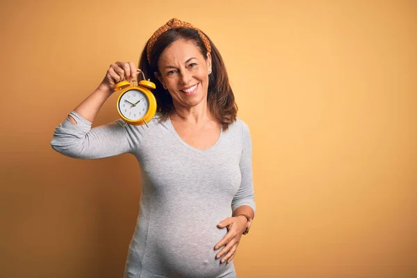 中年妊娠中の赤ちゃんを期待します妊娠ホールディング目覚まし時計で幸せな顔立ちと笑顔で自信を持って笑顔を示す歯 — ストック写真