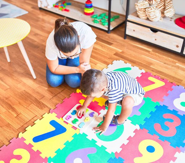 Красивая учительница и малыш сидят на головоломке, играя с цифрами в детском саду

