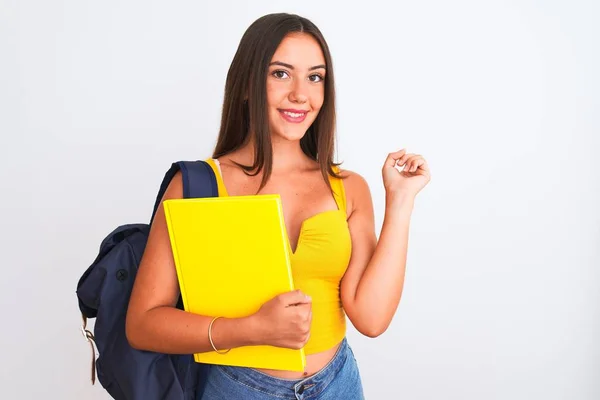 漂亮的女学生背着背包 把笔记本放在孤立的白色背景上 手指手画脚地指着旁边 非常开心 — 图库照片