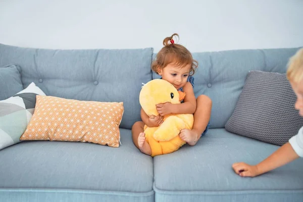 可爱的蹒跚学步的孩子笑得很开心 坐在沙发上玩家里的鸭娃娃 — 图库照片