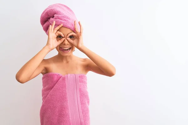 漂亮的小女孩洗完澡后穿着浴巾站在孤立的白色背景上做着像双筒望远镜一样的手势 伸出舌头 眼睛透过手指看着 疯狂的表情 — 图库照片