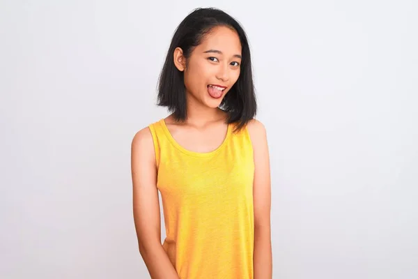 黄色のカジュアルなTシャツを着た若い中国人女性が 独立した白い背景の上に立って 面白い表情で幸せに舌を突き出しています 感情概念 — ストック写真