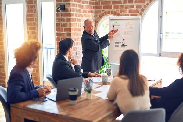 Group of business workers smiling happy and confident in a meeting. Working together looking at presentation using board and charts at the office.