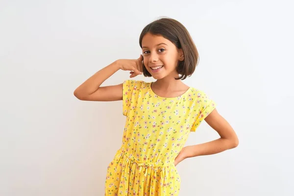 年轻美丽的小女孩穿着黄色的花裙子 站在孤独的白色背景上 微笑着用手和手指做着电话手势 就像在电话里说话一样 交流概念 — 图库照片