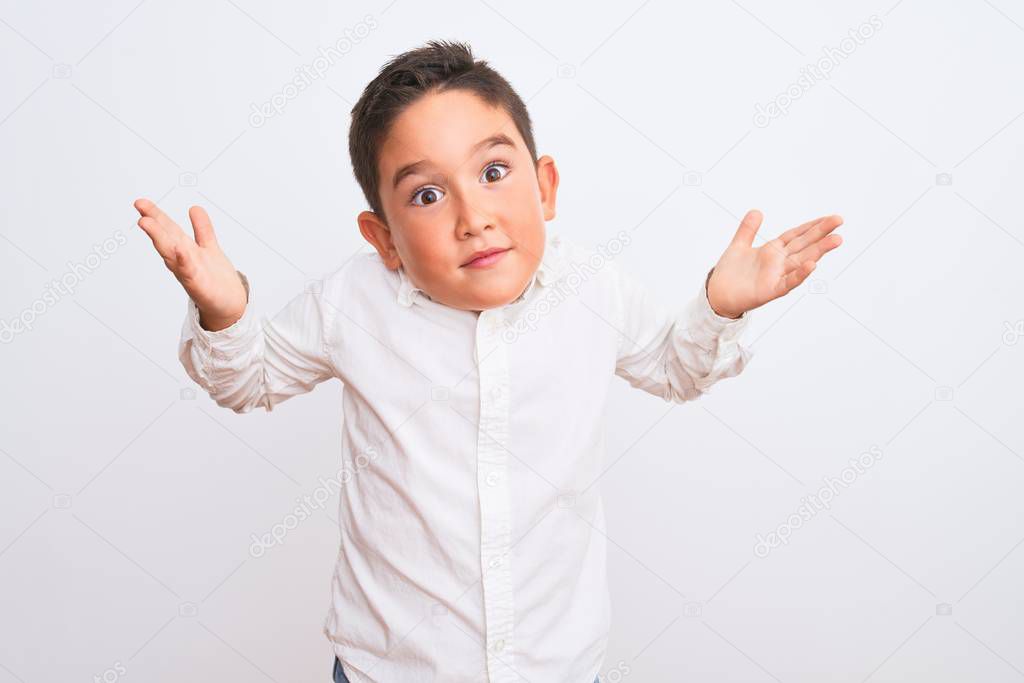 Beautiful kid boy wearing elegant shirt standing over isolated white background clueless and confused expression with arms and hands raised. Doubt concept.