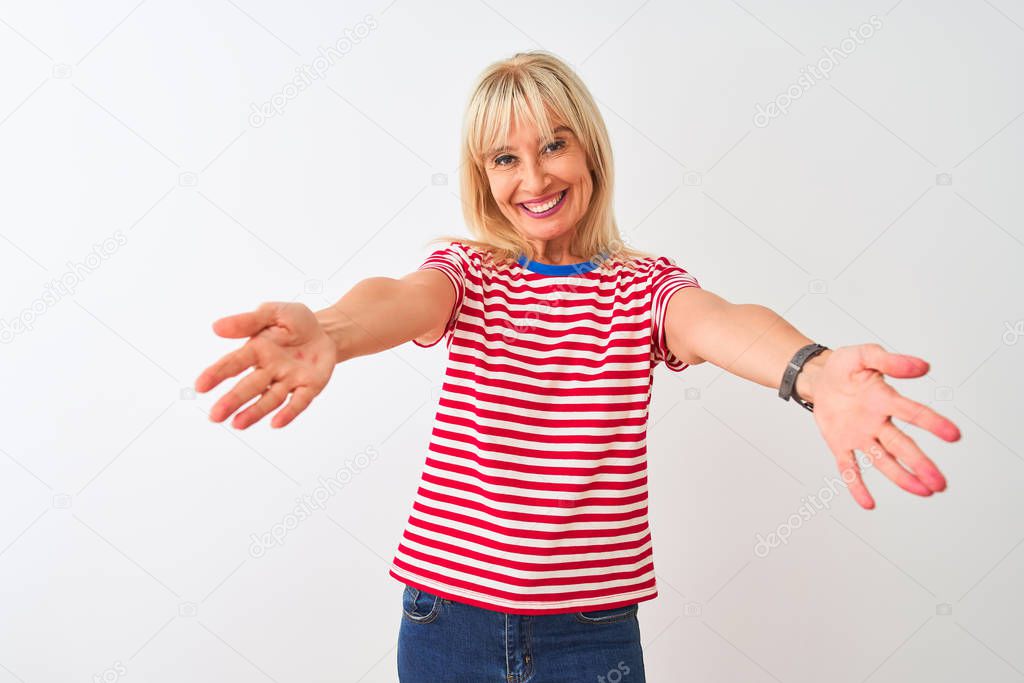 Middle age woman wearing casual striped t-shirt standing over isolated white background looking at the camera smiling with open arms for hug. Cheerful expression embracing happiness.