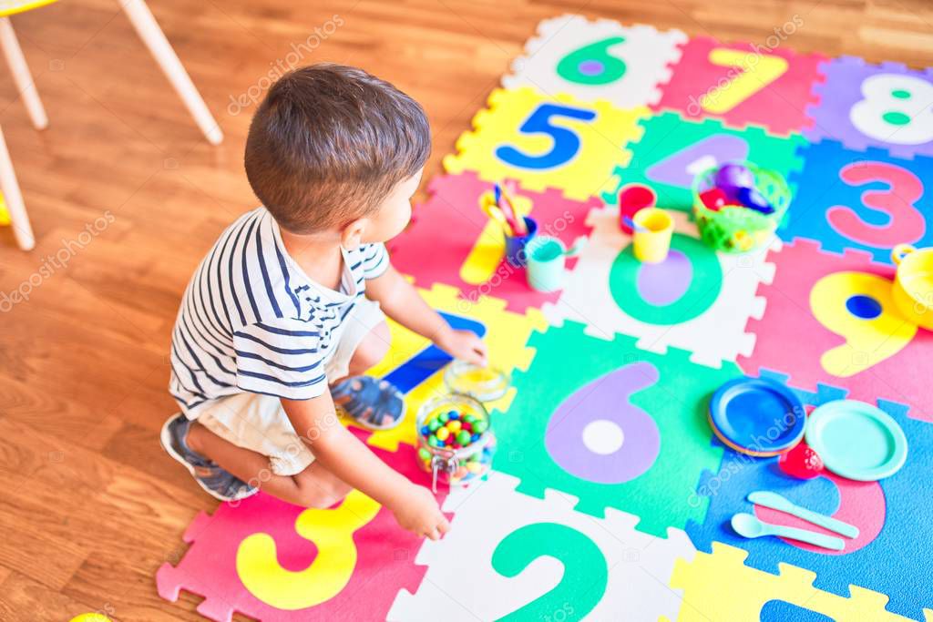 Beautiful toddler boy sitting on puzzle eating small colored chocolate balls at kindergarten