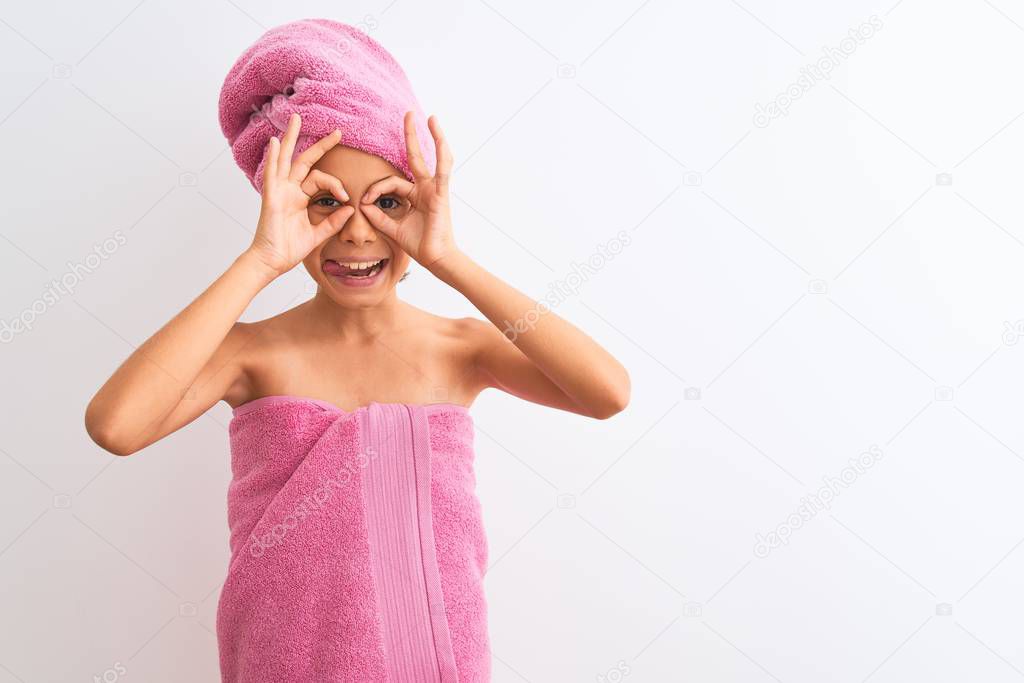 Beautiful child girl wearing shower towel after bath standing over isolated white background doing ok gesture like binoculars sticking tongue out, eyes looking through fingers. Crazy expression.