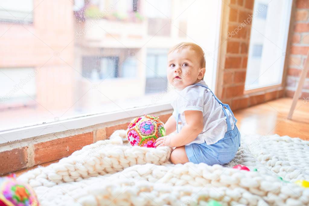 Beautiful toddler sitting on the blanket looking through the window at kindergarten