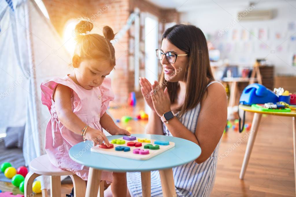 Young beautiful teacher and toddler learning maths playing with numbers puzzle at kindergarten