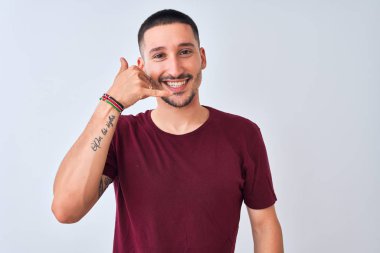 Genç yakışıklı adam izole edilmiş arka planda durup gülümsüyor telefonla el ve parmaklarıyla telefon hareketi yapıyor telefonda konuşuyor gibi. İletişim kavramları.