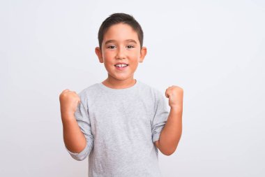 Gri günlük tişört giyen güzel çocuk, izole edilmiş beyaz arka planda durup kollarını kaldırarak ve açık gözlerle başarıyı kutluyor ve şaşırıyor. Kazanan konsept.