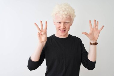 Siyah tişörtlü genç albino adam izole edilmiş beyaz arka planda duruyor ve 8 numaralı parmaklarıyla gülümseyerek kendinden emin ve mutlu görünüyor..
