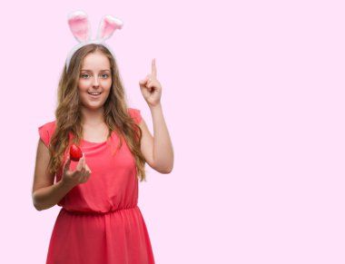 Sarışın genç kadın giyiyor Paskalya bunny kulaklar bir fikir ya da soru işaret parmağı ile gülen yüz, sürpriz bir numara