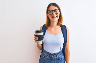 Beautiful redhead student woman wearing a backpack and drinking take away coffee with a happy face standing and smiling with a confident smile showing teeth