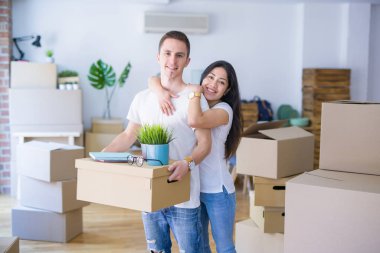 Young beautiful couple sitting on the floor at new home around cardboard boxes celebrating surprised and amazed for success with arms raised and open eyes. Winner concept.