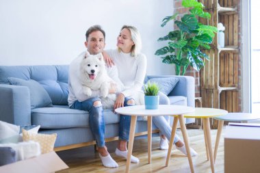 Karton kutular etrafında yeni evde kanepede oturan köpek ile genç güzel çift