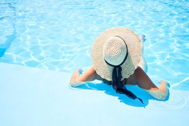 Tatil günü havuzda yüzen, güneşli bir günde suda güneşlenen güzel ve seksi bir kadın.
