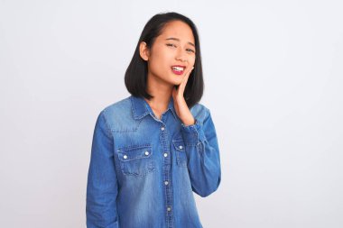 Young beautiful chinese woman wearing denim shirt standing over isolated white background touching mouth with hand with painful expression because of toothache or dental illness on teeth. Dentist concept.