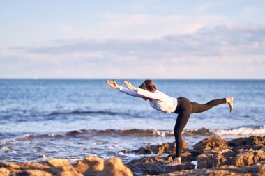 Genç yakışıklı sporcu yoga yapıyor. Koç kumsalda savaşçı pozu veriyor.