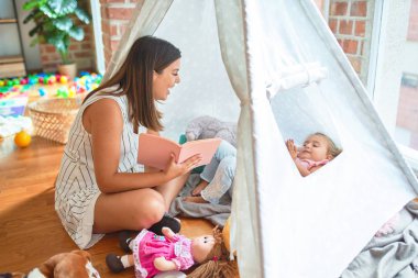 Anaokulunda Tip 'in içinde yerde yatan sarışın kıza güzel bir öğretmen kitabı okuyor.