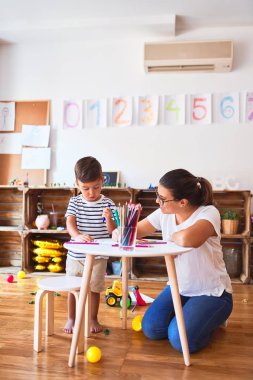 Güzel öğretmen ve çocuk anaokulunda renkli kalemlerle resim çiziyor.