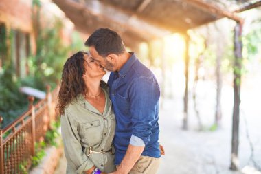 Şehir parkında mutlu ve kendinden emin gülümseyen orta yaşlı güzel bir çift. Yüzünde gülümsemeyle ayakta durup sarılıp öpüşmek.