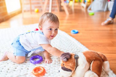 Güzel çocuk, anaokulunda battaniyeye oturmuş oyuncak köpekle oynuyor.