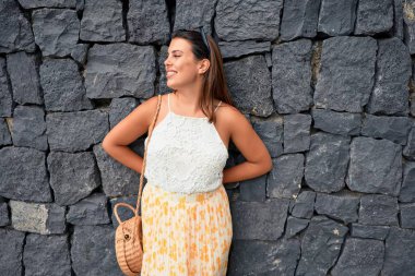 Güzel kız duvara yaslanıyor, genç arkadaş canlısı kadın mutlu bir yaz gününde gülümsüyor.