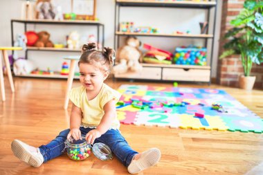 Anaokulunda elinde bir kavanoz çikolata renkli topla yerde oturan güzel çocuk.