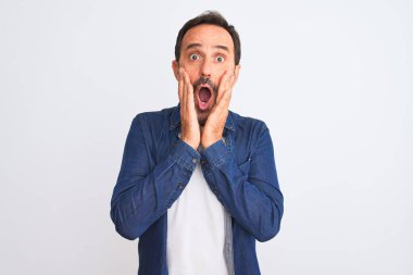 Mavi kot gömlek giyen orta yaşlı yakışıklı bir adam izole edilmiş beyaz arka plan üzerinde duruyor korkmuş ve şok olmuş, şaşırmış ve şaşırmış bir yüz ifadesi var.