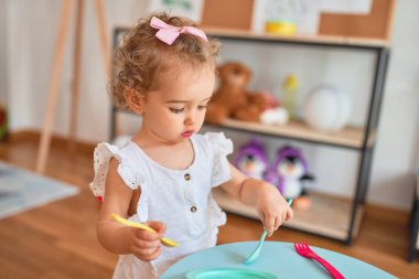 Renkli oyun odasında beyaz güzel bir bebek oyuncaklarla oynuyor. Anaokulundaki sahte mutfakta mutlu ve eğlenceli yemekler..