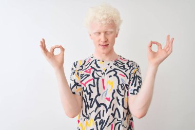 Renkli tişört giyen genç albino adam izole edilmiş beyaz arka planda duruyor rahatla ve gözleri kapalı meditasyon yaparken parmaklarıyla gülümse. Yoga konsepti.