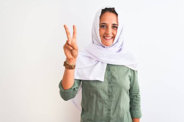 Geleneksel Müslüman tesettürlü genç, güzel bir Arap kadını izole edilmiş arka planda iki numaralı parmaklarıyla işaret ederken kendinden emin ve mutlu bir şekilde gülümsüyor..