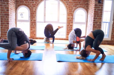 Genç ve güzel bir grup sporcu kadın yoga yapıyor. Koç, spor salonundaki kadınlara karga pozu veriyor.