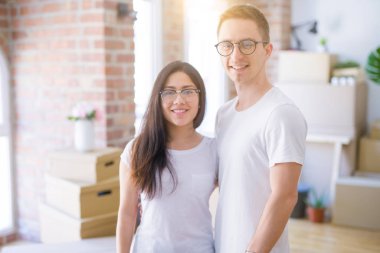 Young beautiful couple sitting on the floor at new home around cardboard boxes celebrating surprised and amazed for success with arms raised and open eyes. Winner concept.