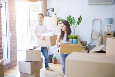 Young beautiful couple sitting on the floor at new home around cardboard boxes celebrating surprised and amazed for success with arms raised and open eyes. Winner concept.