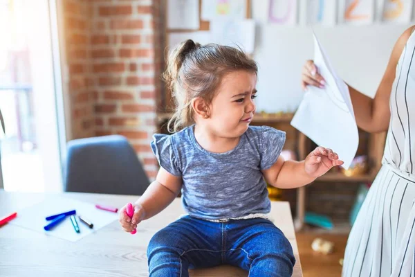 Schönes Kleinkind Sitzt Weinend Schreibtisch Und Junge Lehrerin Zeigt Zeichnung — Stockfoto