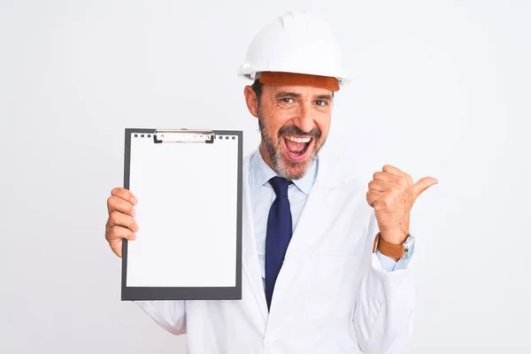 高级工程师头戴安全帽 手持剪贴板 在孤立的白色背景上指着 带着快乐的面带微笑站在旁边 — 图库照片