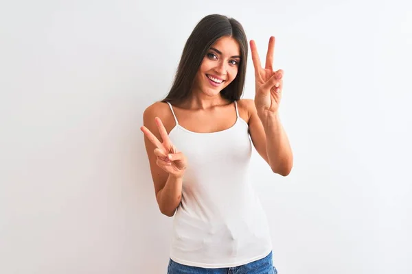 若い美しい女性は 孤立した白い背景の上に立ってカジュアルなTシャツを着て勝利のサインをして指を示すカメラを見て笑っている 第二番 — ストック写真