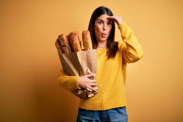 年轻而漂亮的女人提着一袋黄色背景的健康的新鲜面包 担心并强调了一个手牵着额头 紧张而又焦虑的问题 — 图库照片