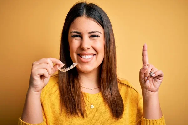 Junge Schöne Frau Mit Zahnkieferorthopädie Korrektor Über Gelbem Hintergrund Überrascht — Stockfoto